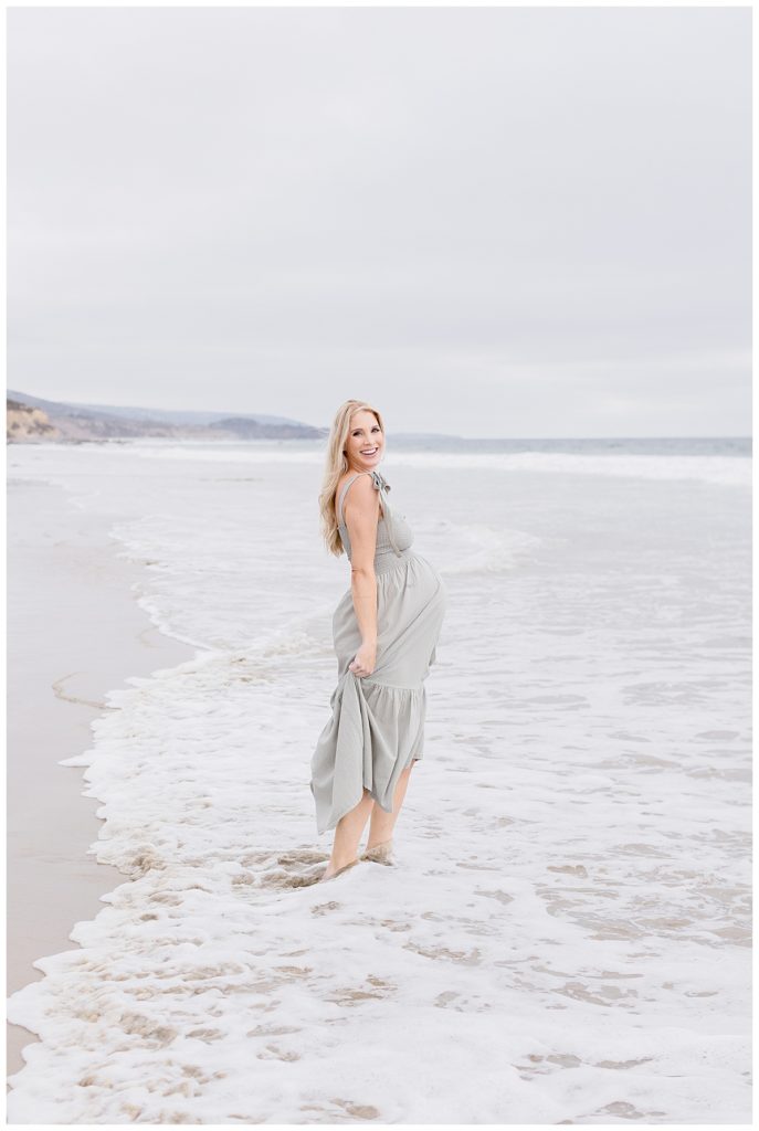 Brenna Proudfoot stands on a beach in Newport for her Maternity Session with Halleigh Hill Orange County Maternity Photographer
