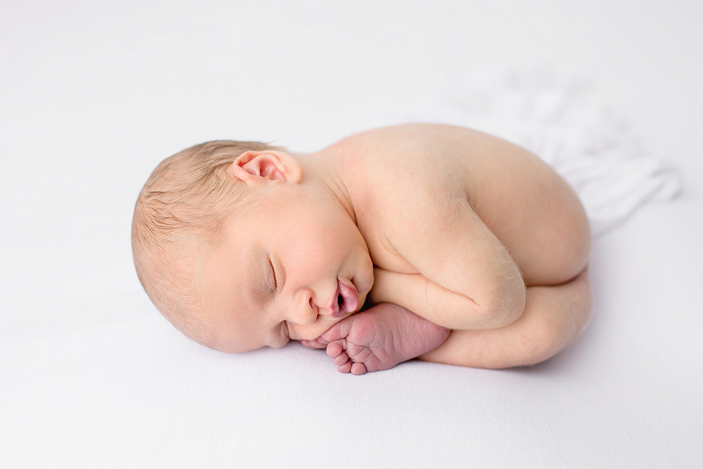 Newborn baby curled up on a white blanket | Image by Halleigh Hill