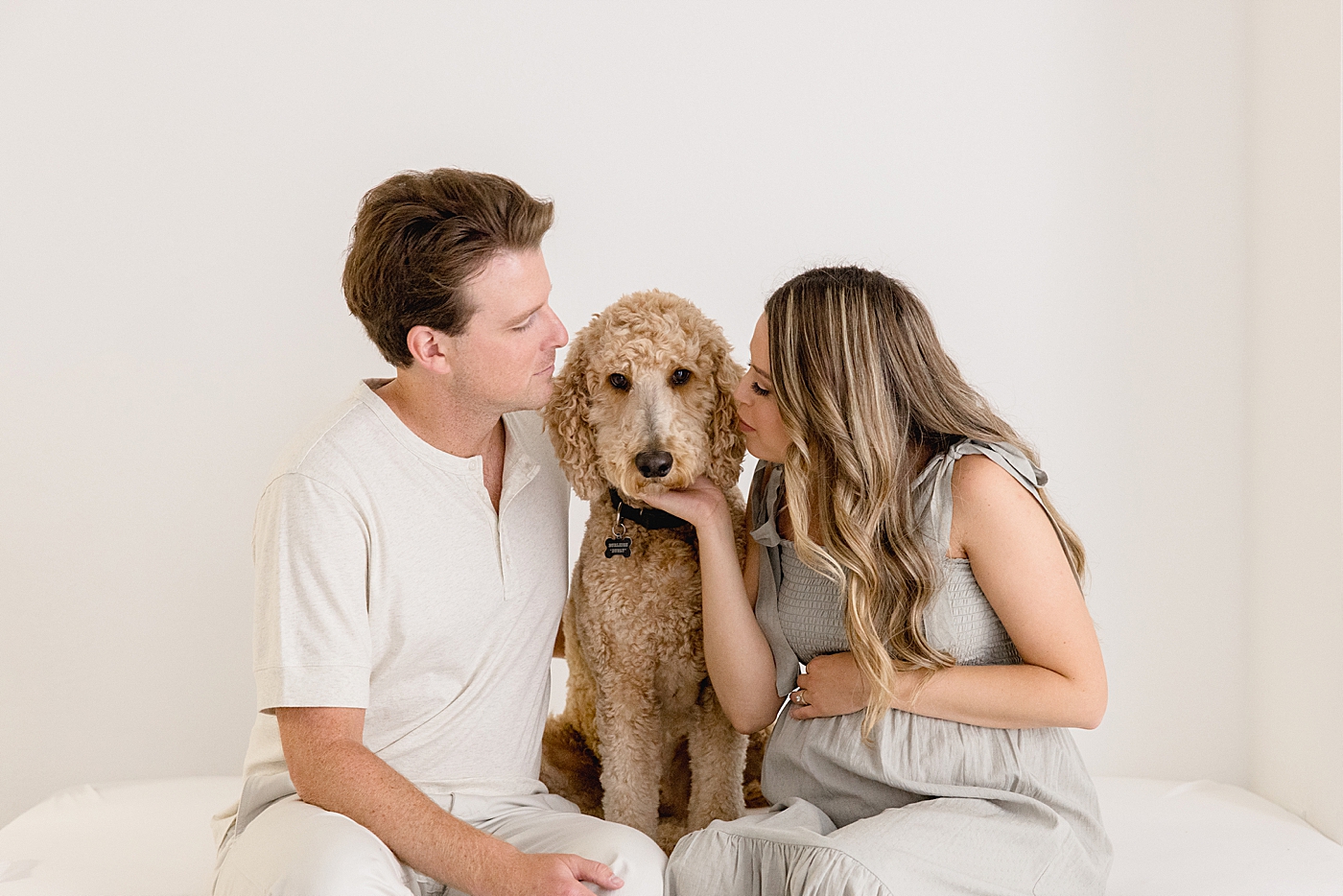 Mom and dad to be sitting on a bed with their dog in the studio | Image by Halleigh Hill