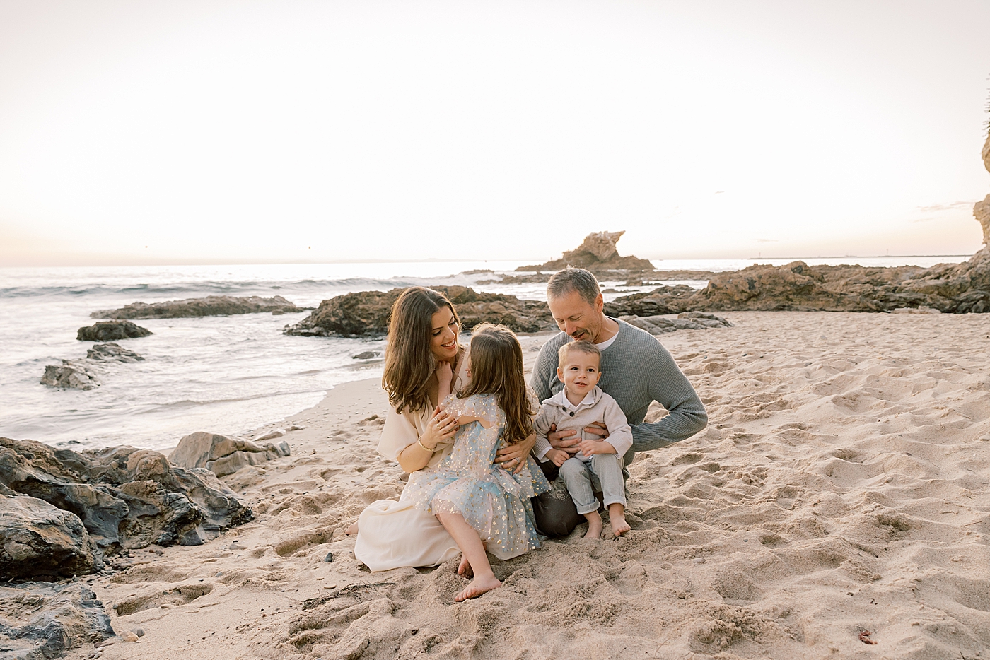 Family snuggling on the beach at sunset in California | Image by Halleigh Hill